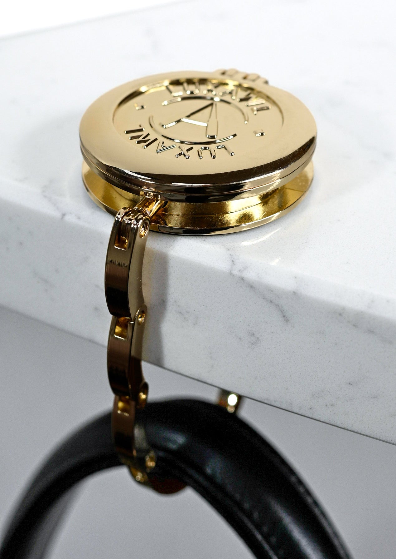 gold bag hook on white marble table with black leather bag hanging from it