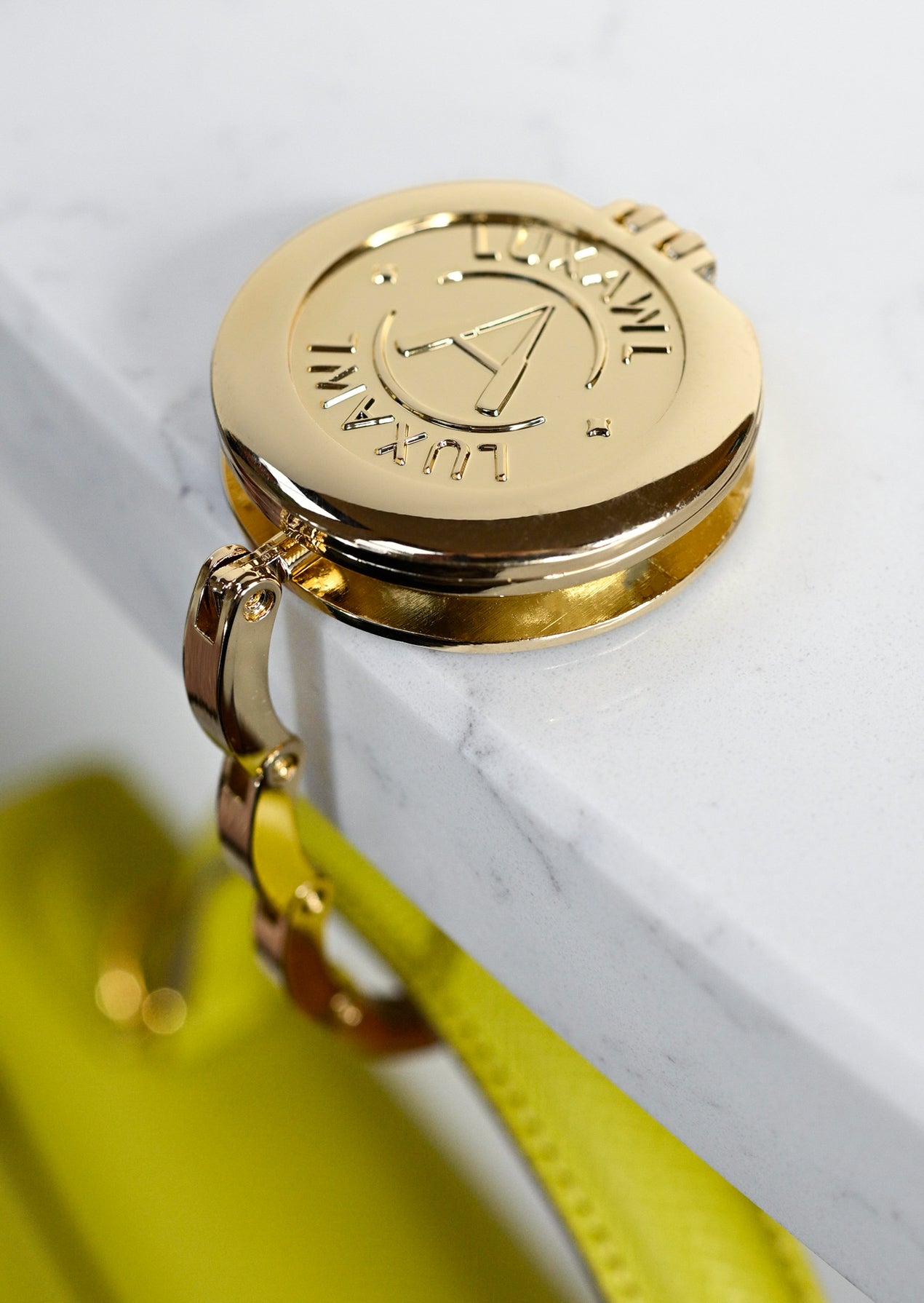 Gold foldable purse hook hanger on white marble table holding a lime yellow bag